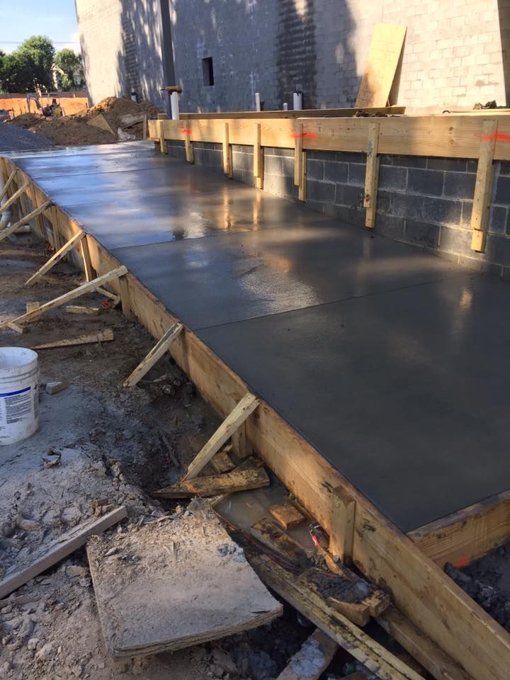 Freshly poured concrete in wooden forms, next to a cinder block wall, outdoors.