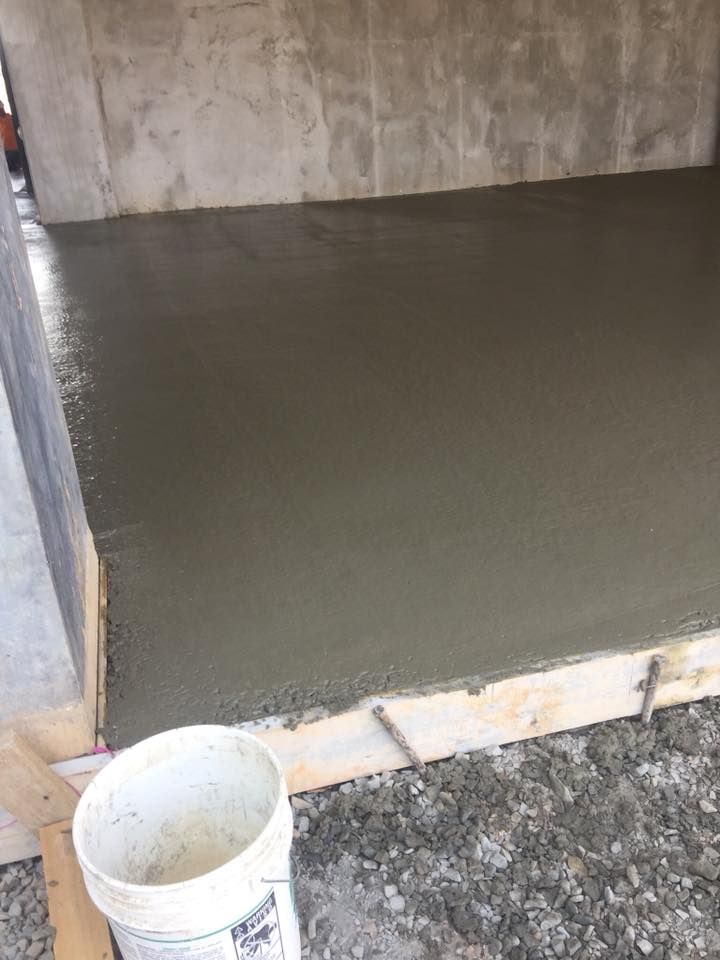 Freshly poured concrete floor in a room, bucket in foreground, gray walls and ground.