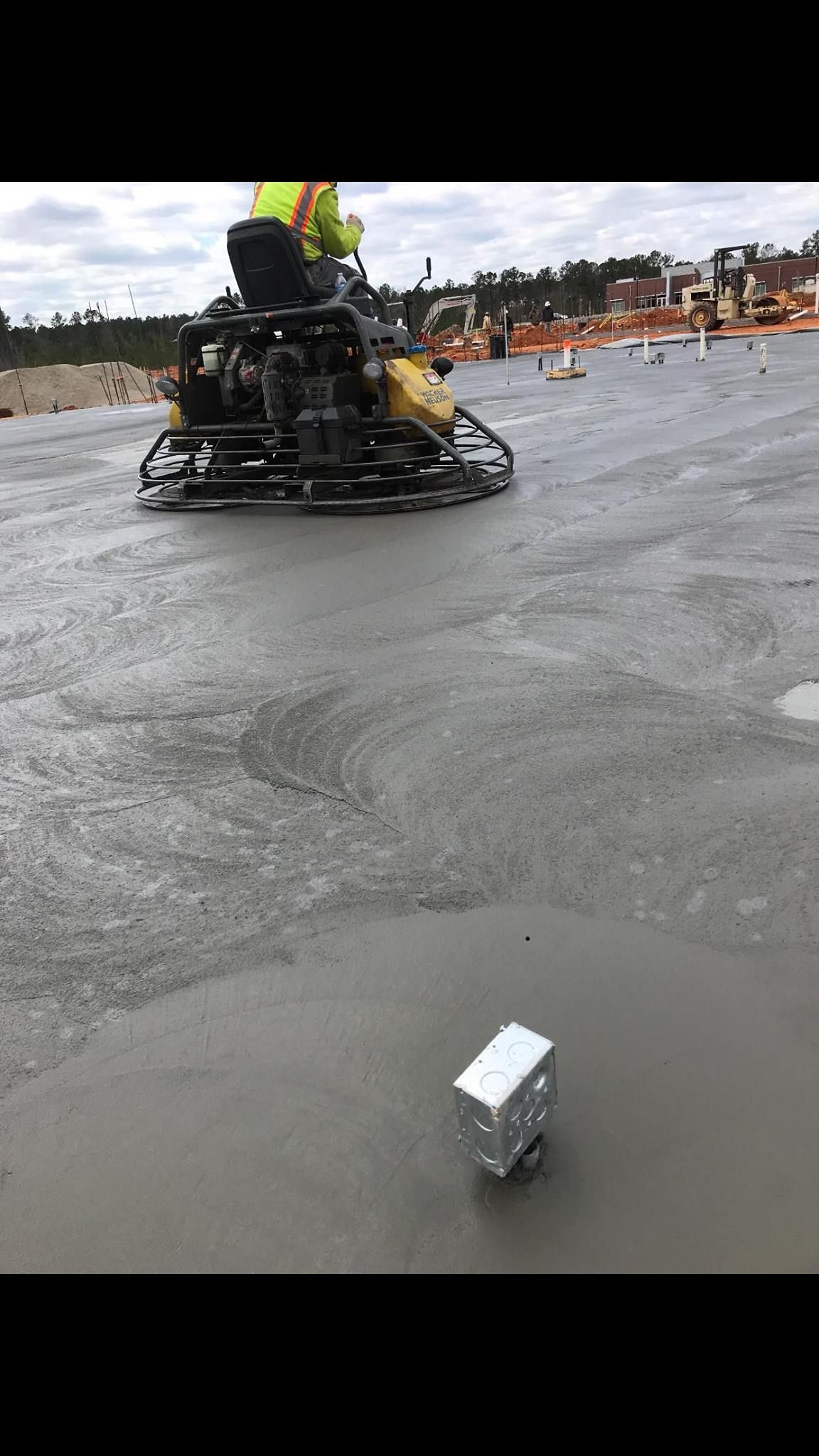 Worker using a concrete finishing machine on a wet concrete surface at a construction site.