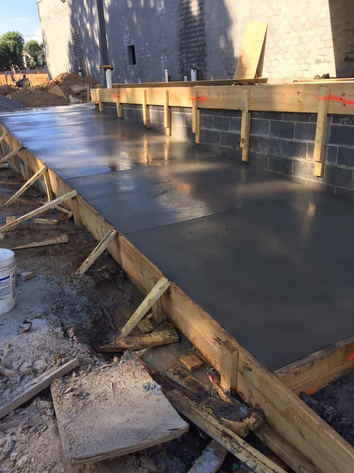 Freshly poured concrete sidewalk with wooden forms, next to a brick wall.