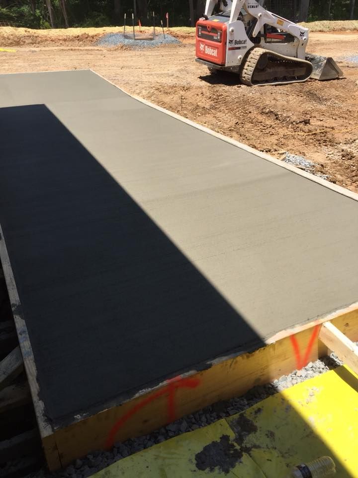 Freshly poured concrete slab in wooden frame at a construction site, with a Bobcat in the background.