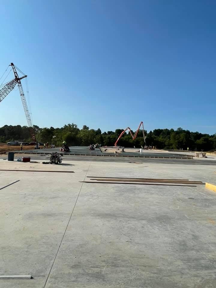 Construction site with a concrete slab, crane, and concrete pump against a blue sky.