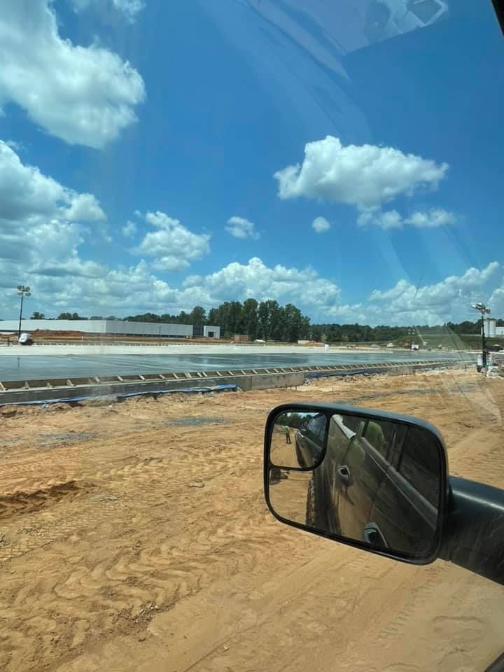 Construction site under a blue sky with fluffy clouds. A side mirror reflects the vehicle and road.
