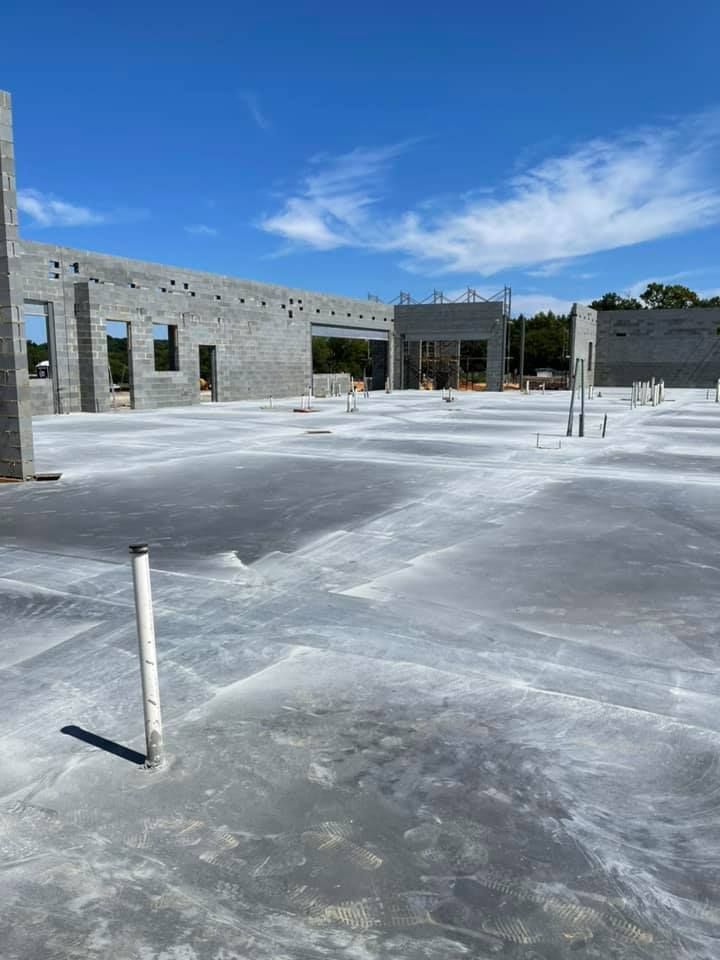 Construction site: concrete floor with pipes and concrete block walls against a blue sky.