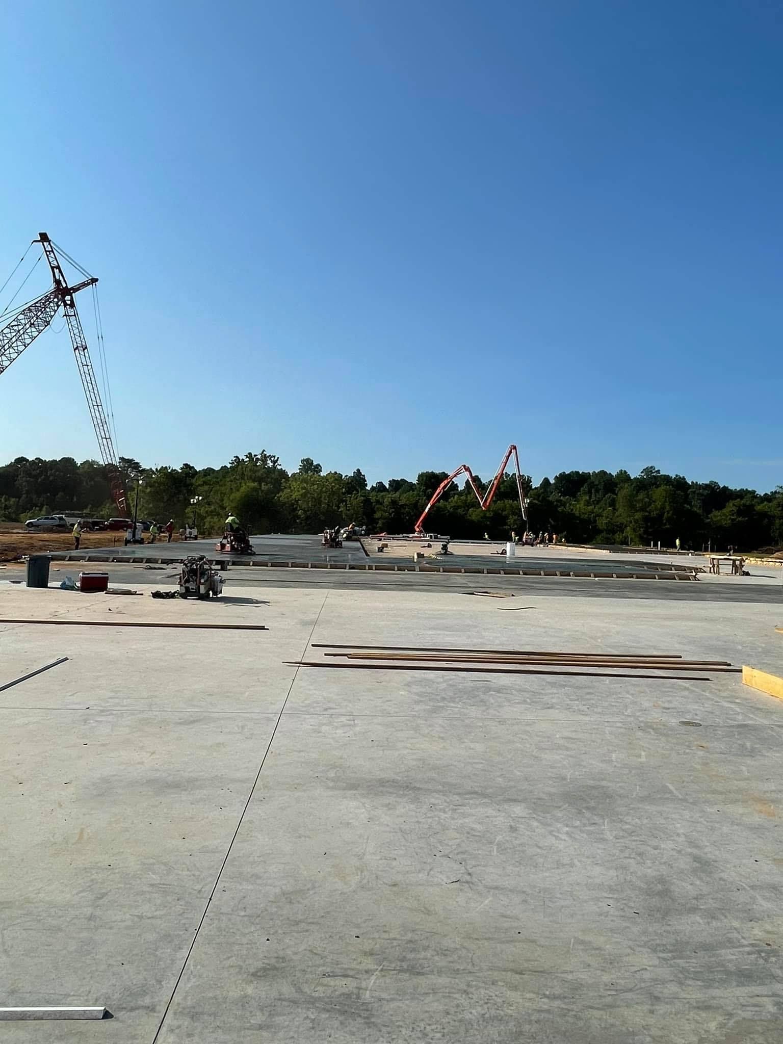 Construction site with concrete floor, trees, blue sky; equipment and workers present.