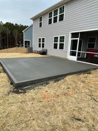 Gray concrete patio next to a two-story gray house with a screened porch on a brown grass lawn.