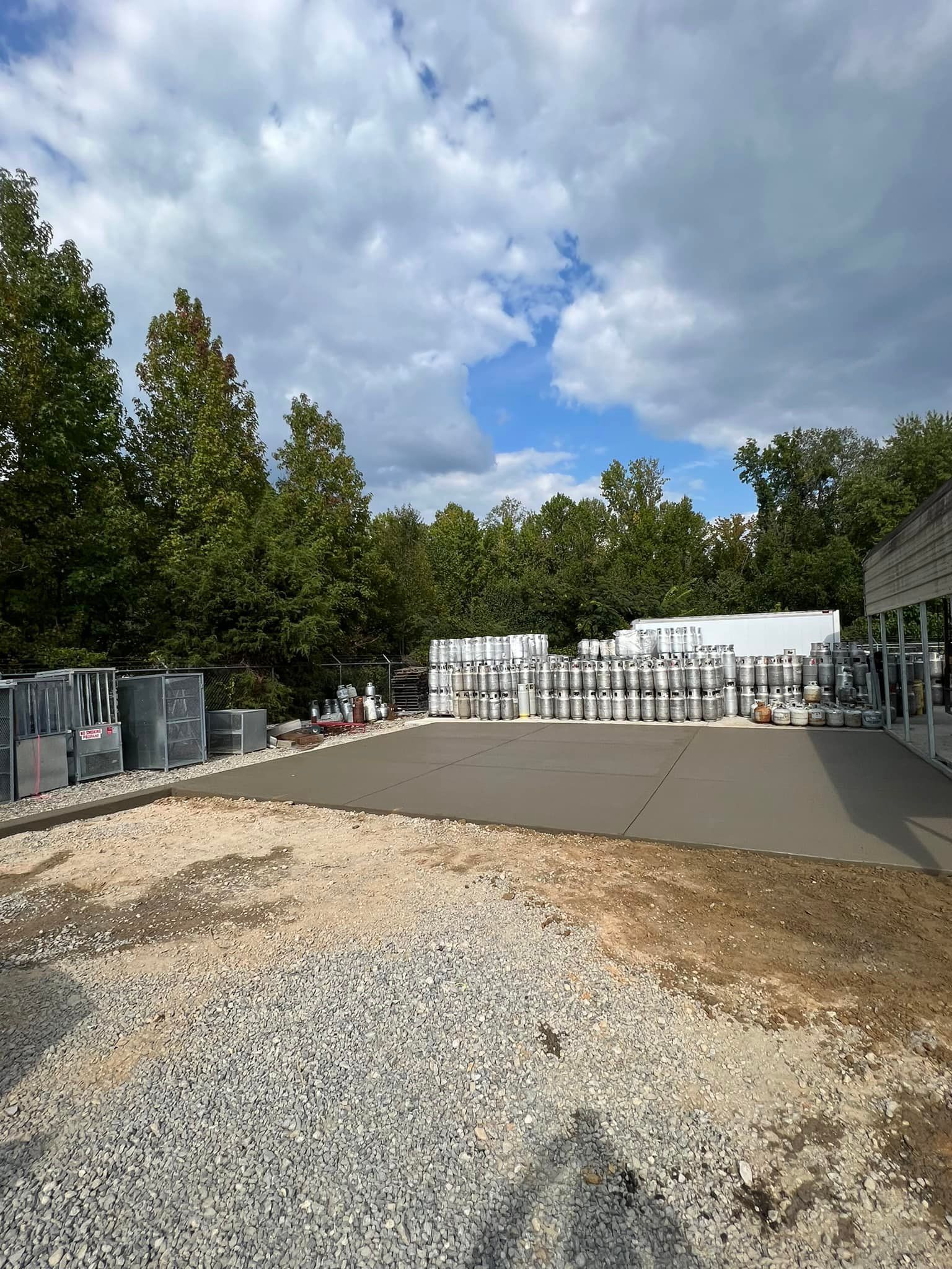 Exterior view of gravel and concrete construction site with trees and overcast sky.