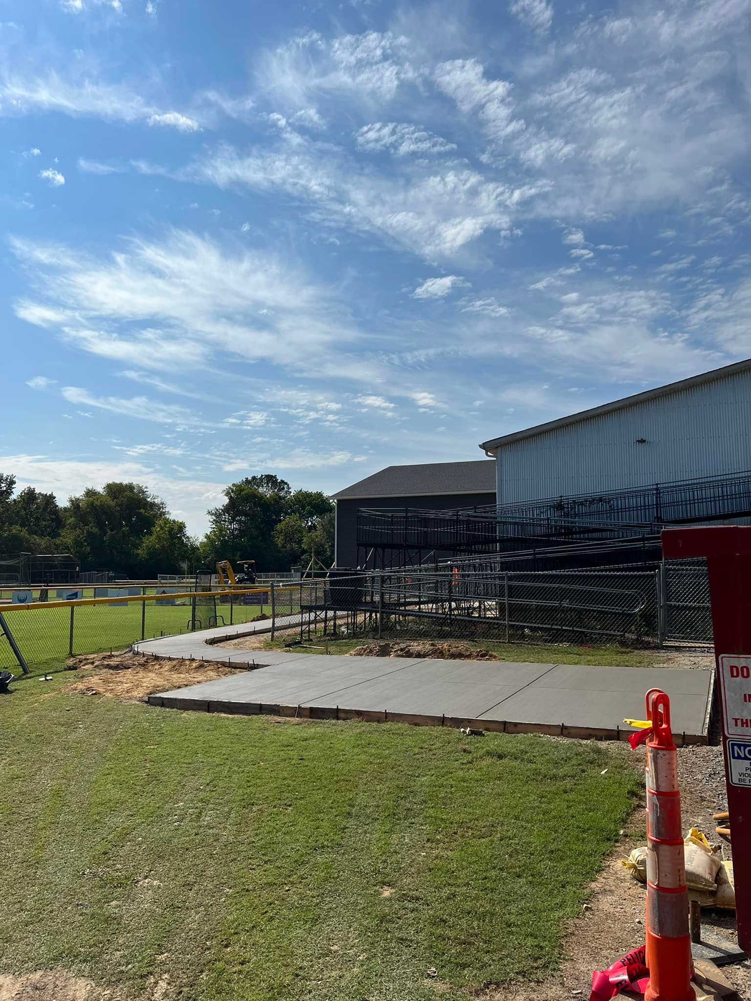 Concrete patio under construction next to a building, on a sunny day with a blue sky and clouds.