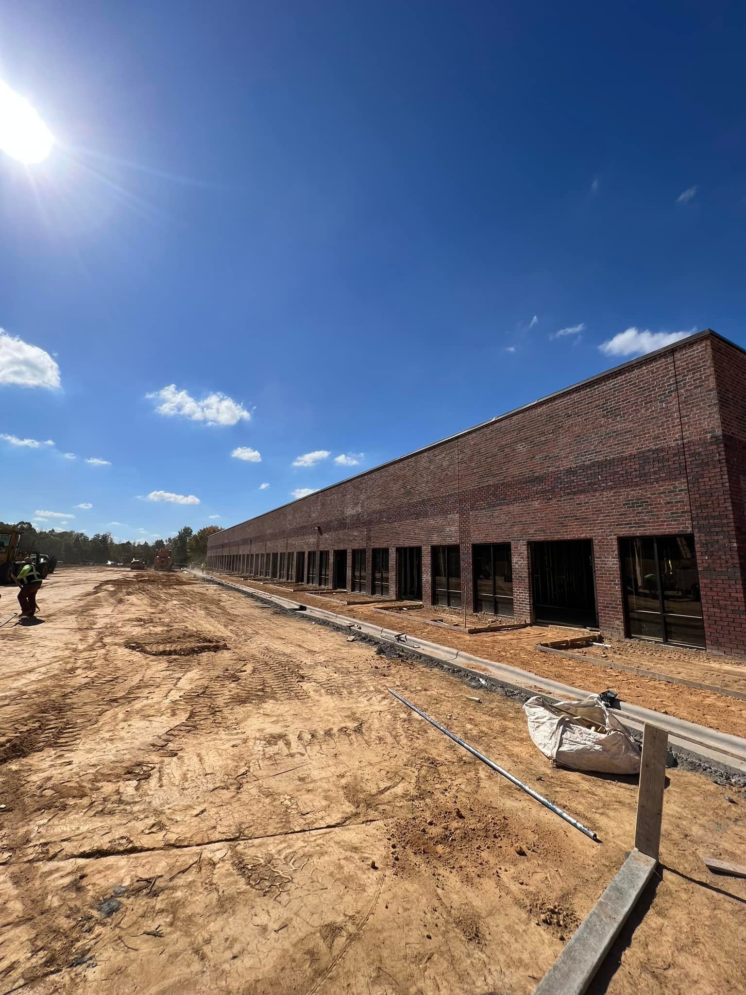 Brick building under construction on a sandy lot, clear blue sky, sunny day.