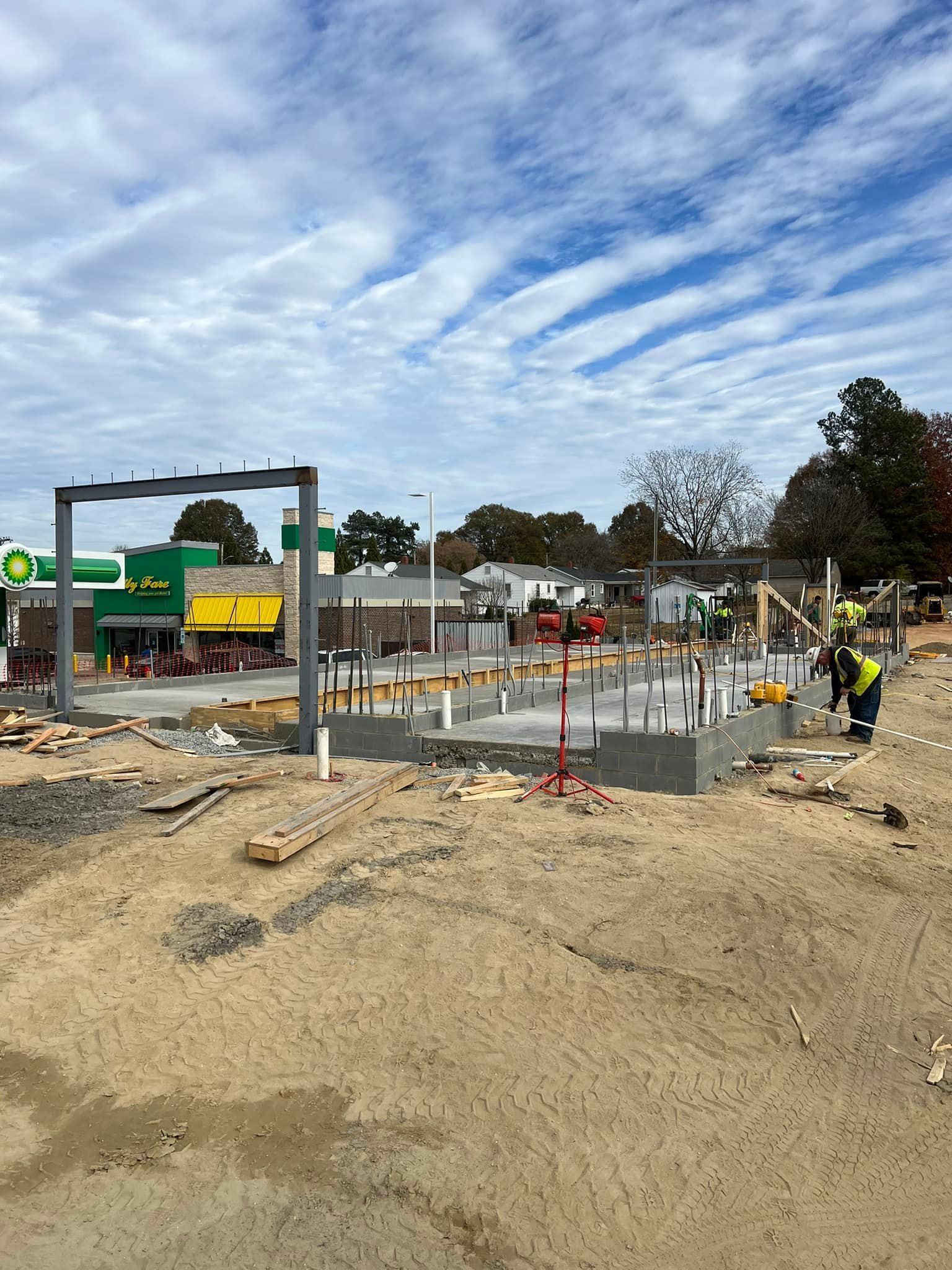 Construction site: new building with steel frame. BP gas station in background. Blue sky, workers present.