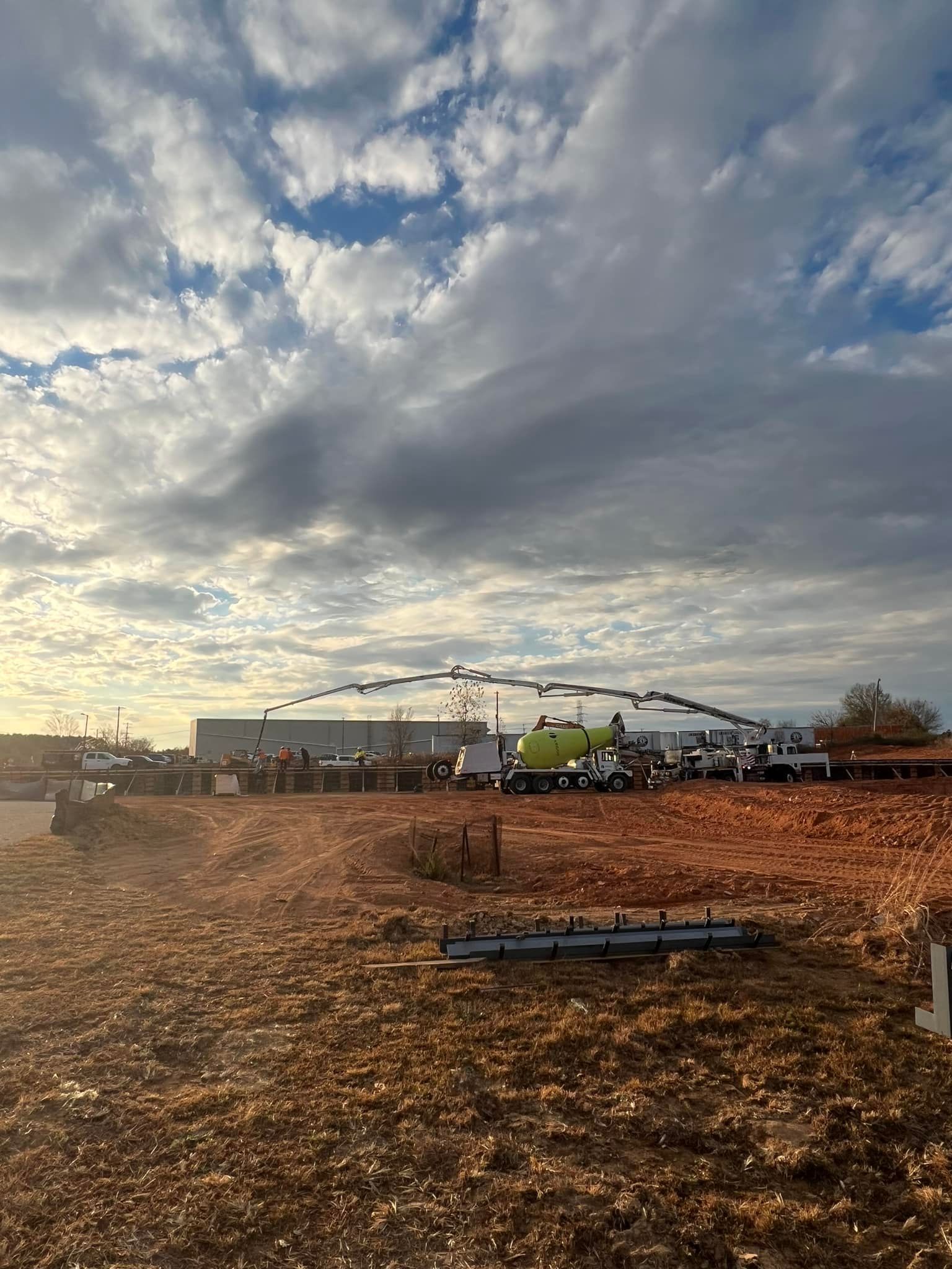 Construction site with a concrete pump truck reaching towards a building under a cloudy sky.