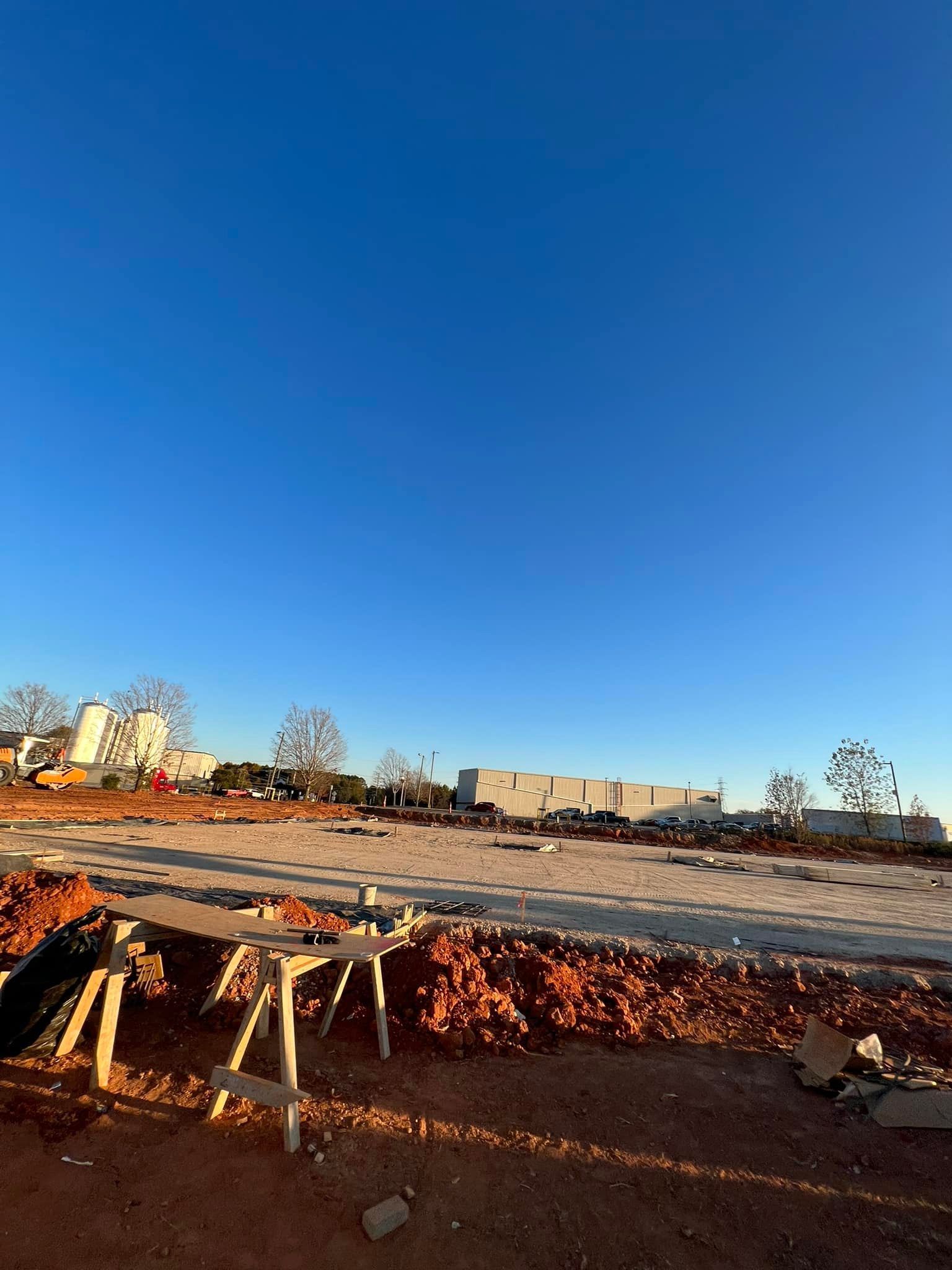 Construction site under a clear blue sky; ground covered in dirt and construction materials.