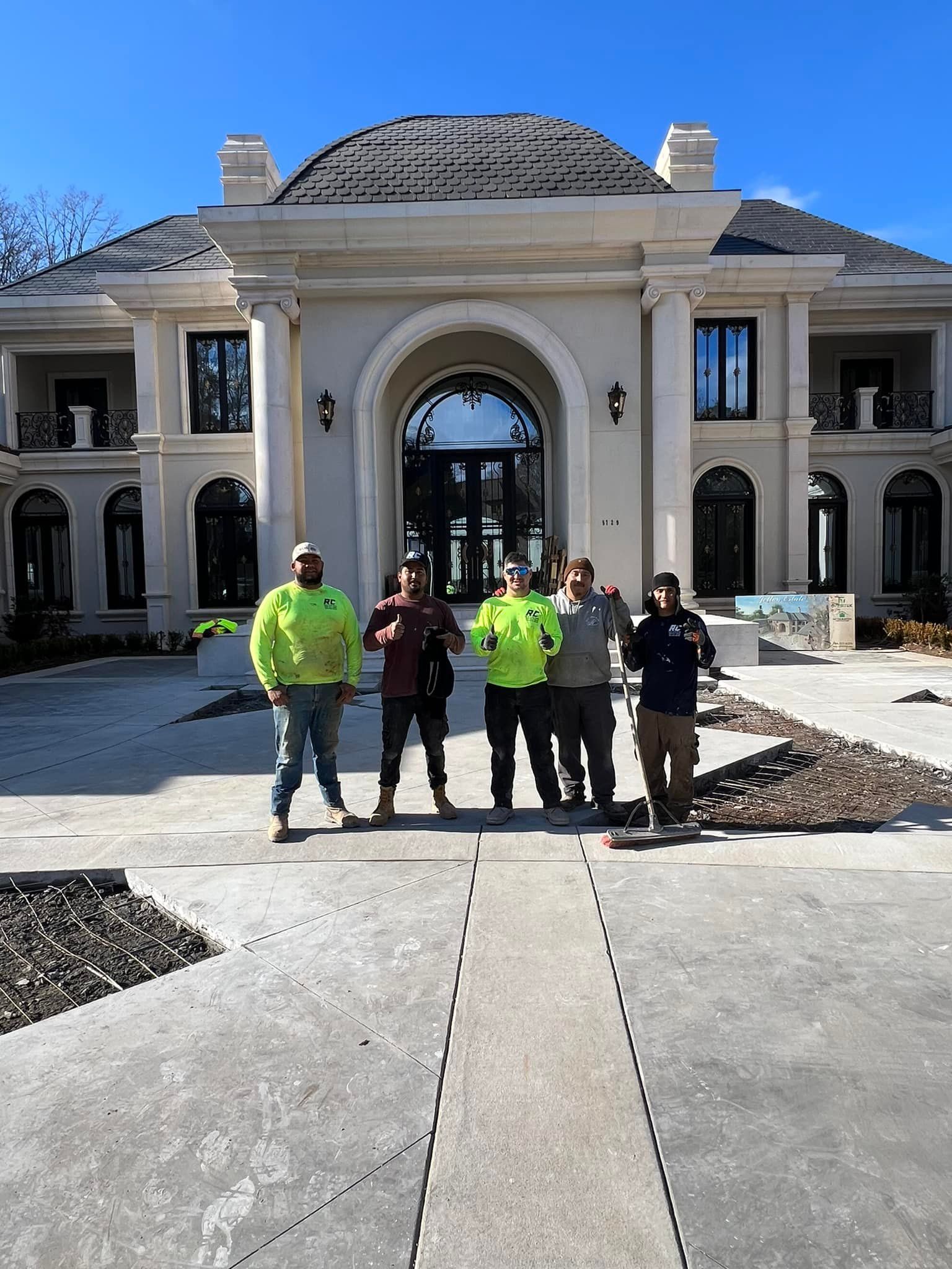 Five construction workers stand in front of a large, elegant house.