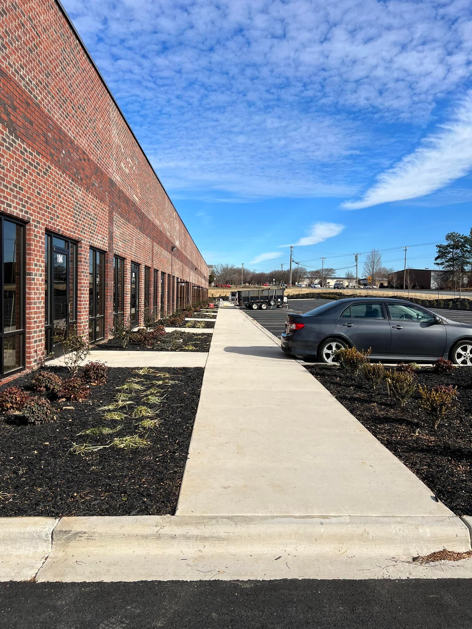 Exterior of a brick building with a sidewalk and a parked car under a blue sky.