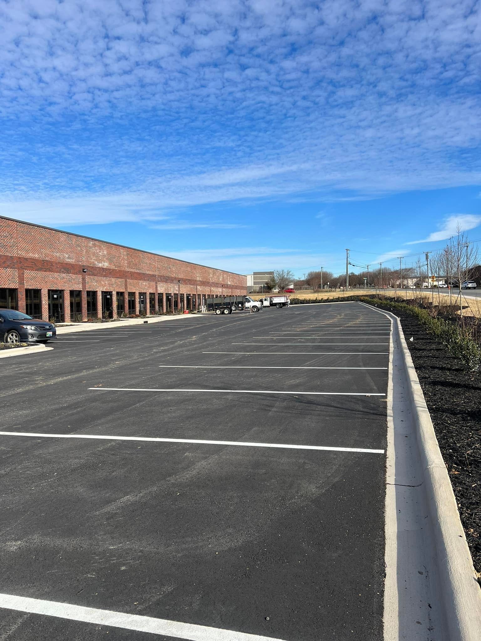 Newly paved parking lot in front of a strip mall with a bright blue sky and some cars parked.