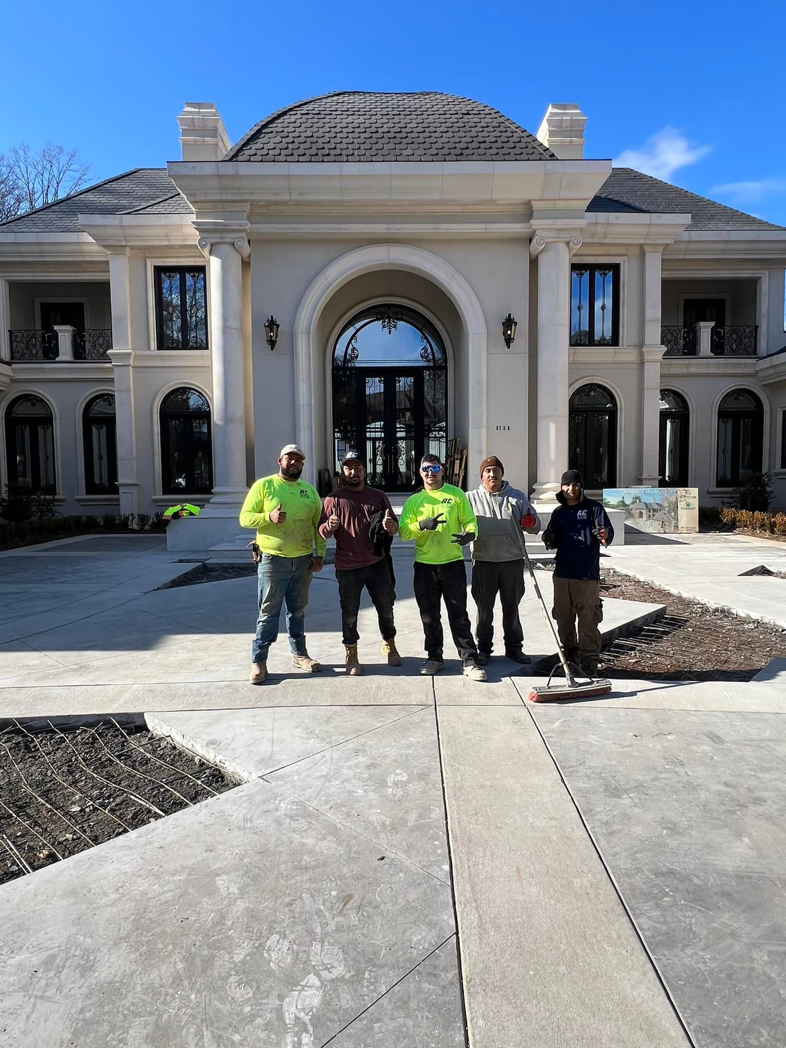 Five construction workers in front of a large, light-colored mansion, smiling.