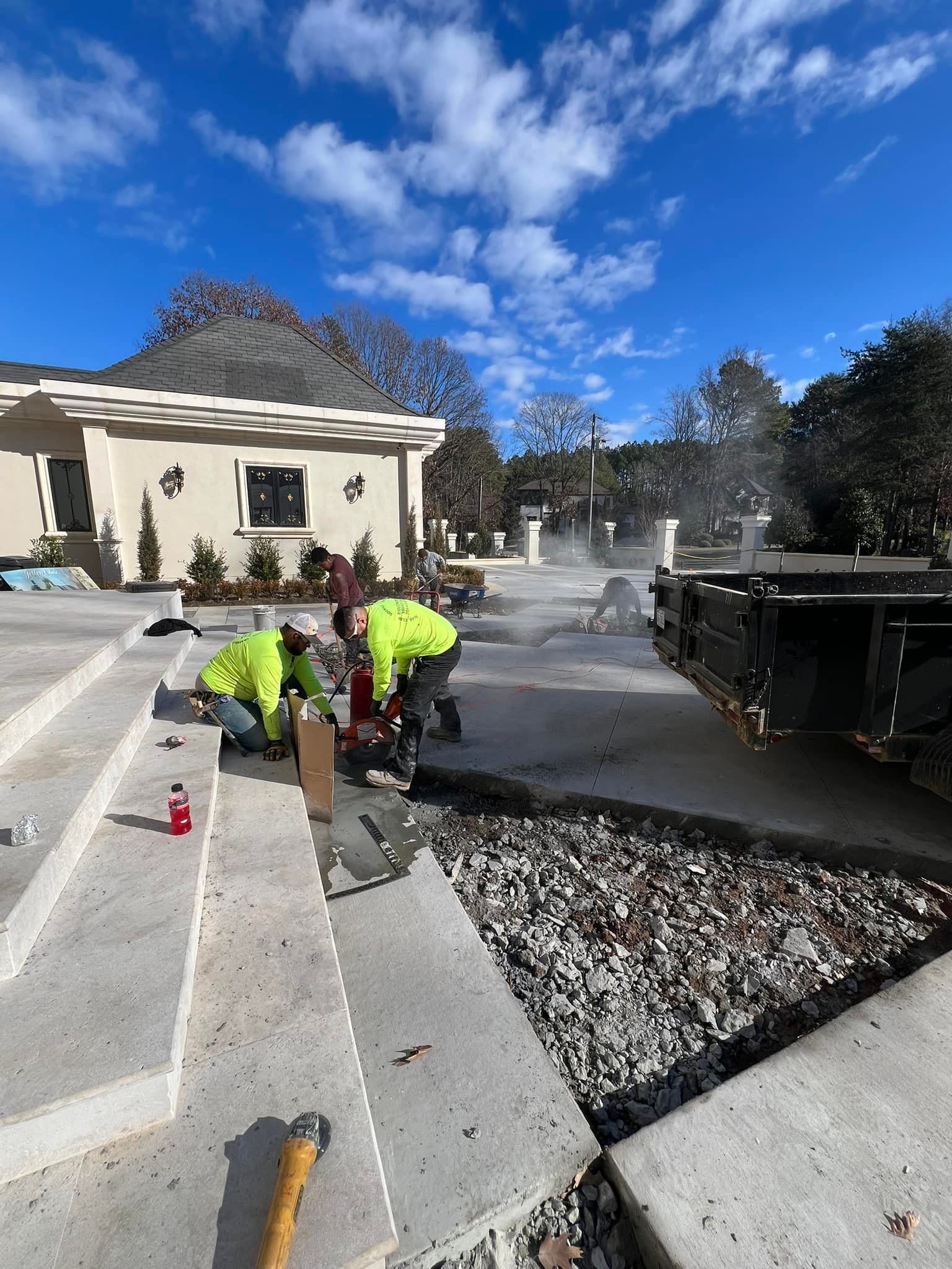 Construction workers in neon vests cutting concrete outside a house with a blue sky.