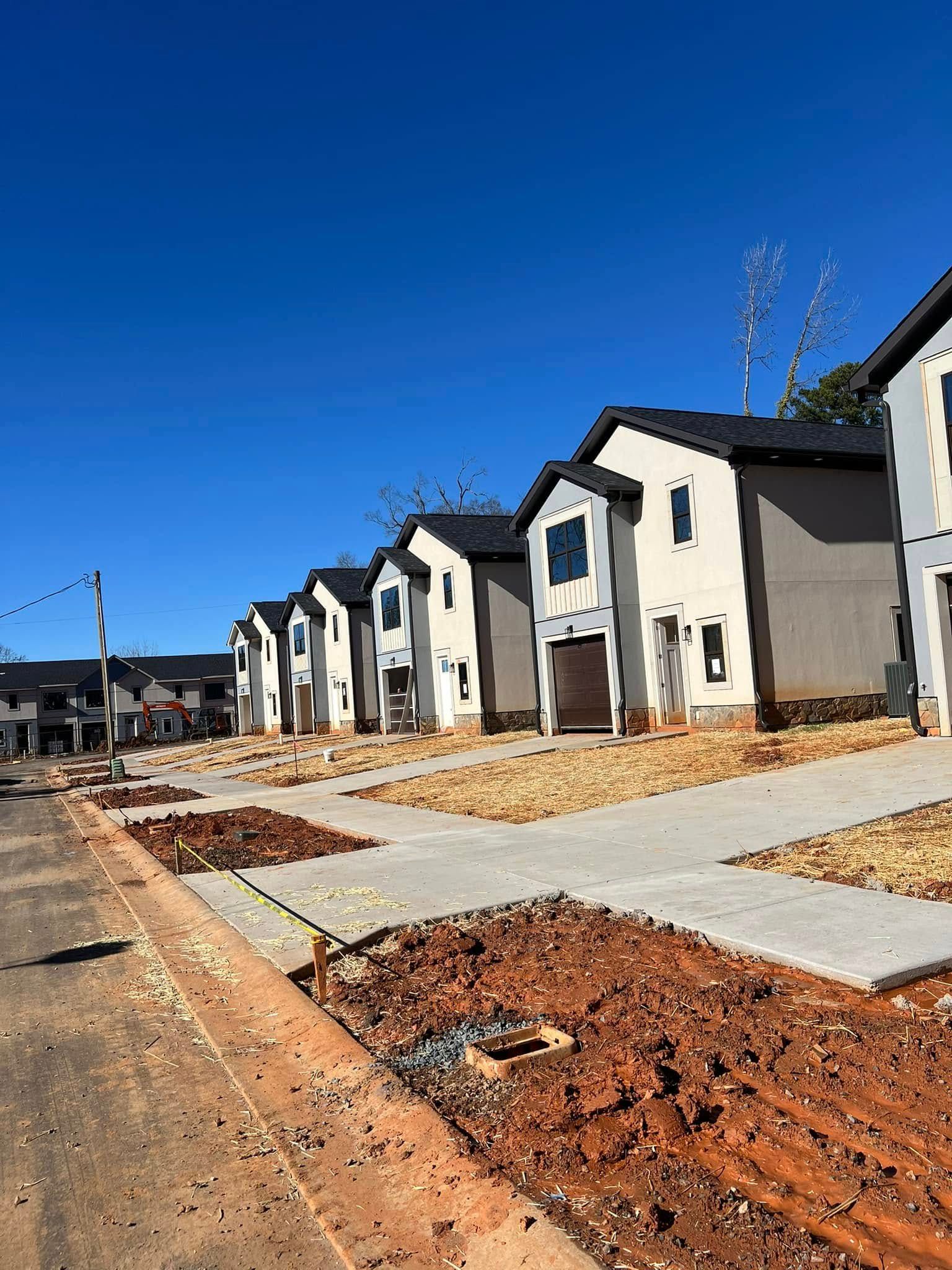 Row of newly-built townhouses with beige siding, dark roofs, on a sunny day.