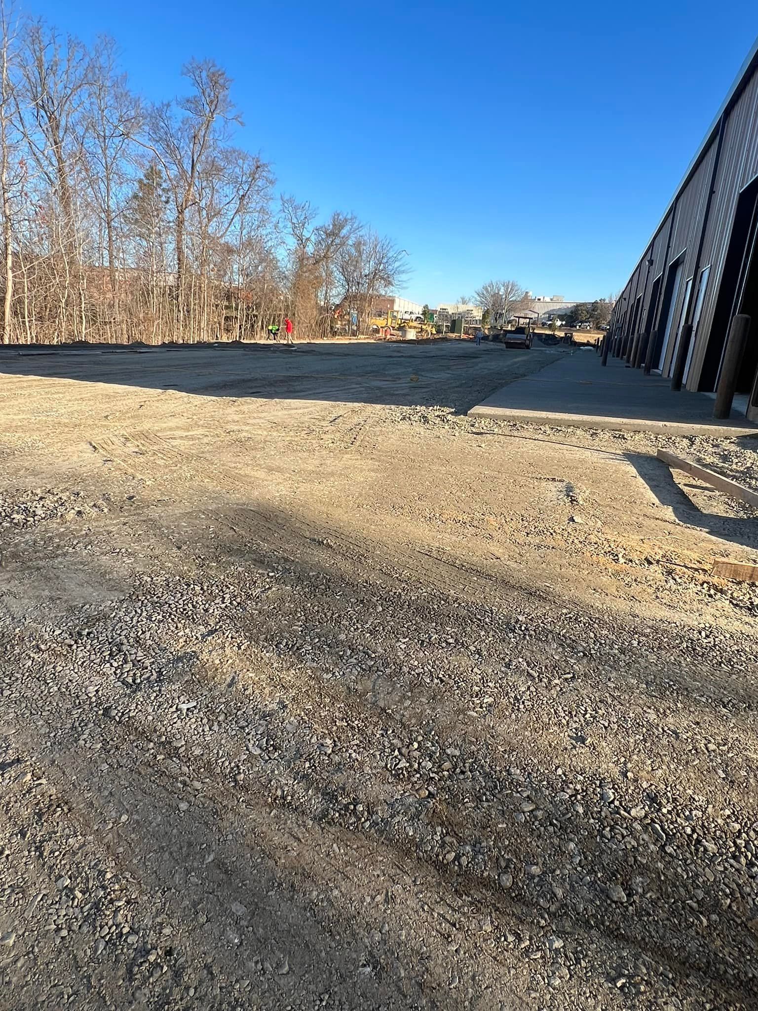 Gravel parking lot next to brick building, trees in the background, clear blue sky.