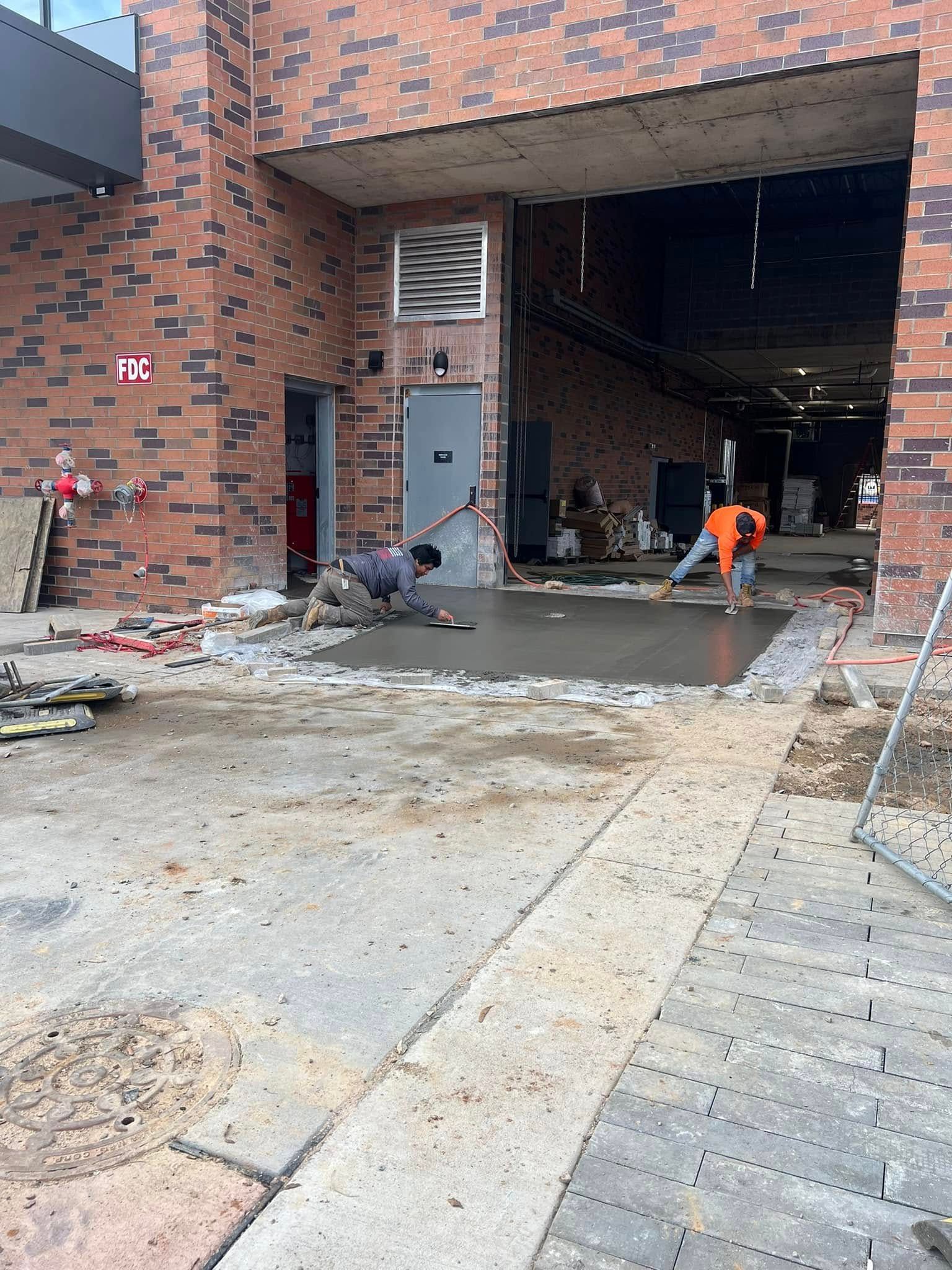 Construction workers smoothing concrete at a building entrance with red brick walls.