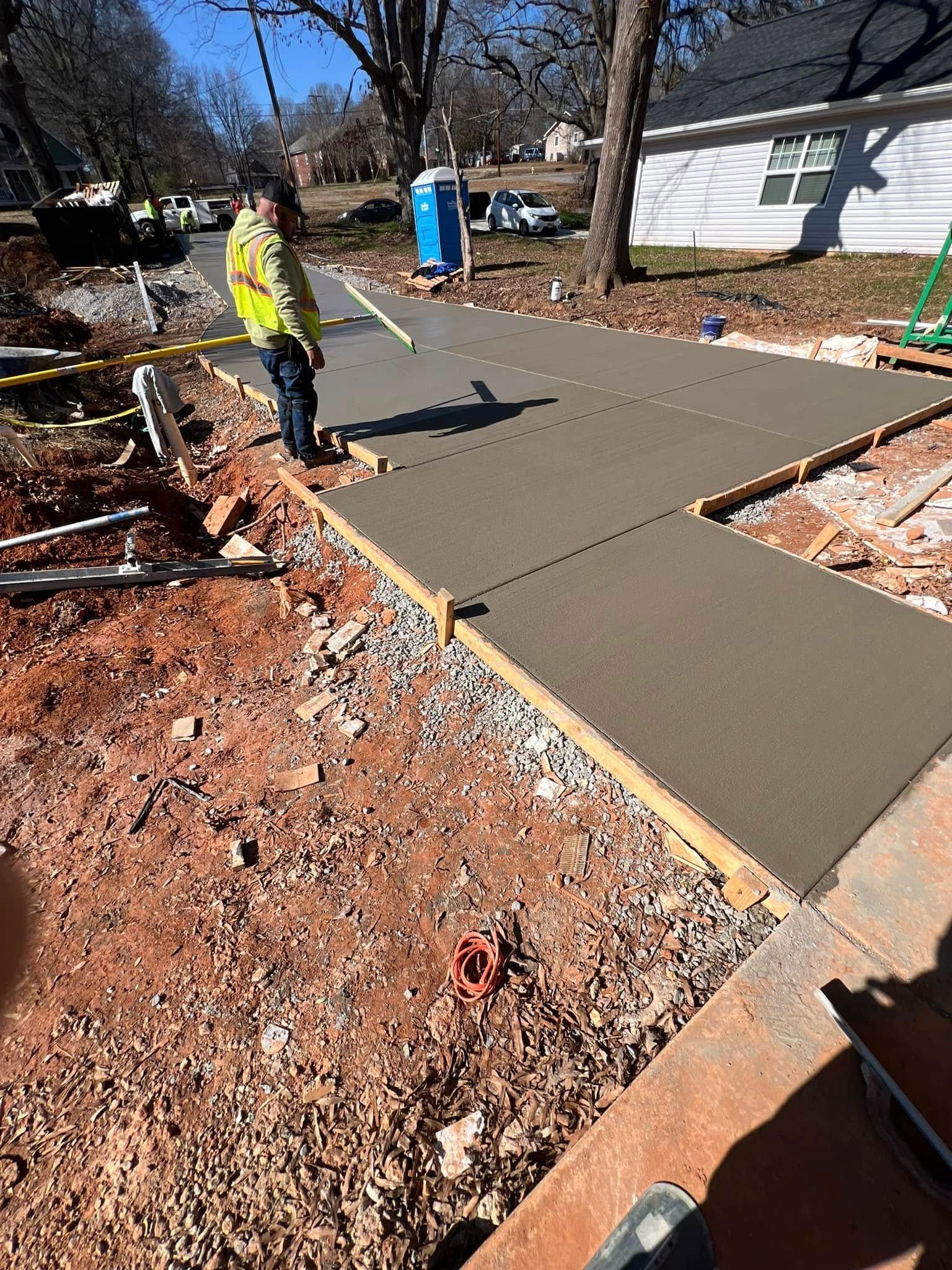 A construction worker using a level to smooth wet concrete on a sidewalk. Outdoors, sunny day.