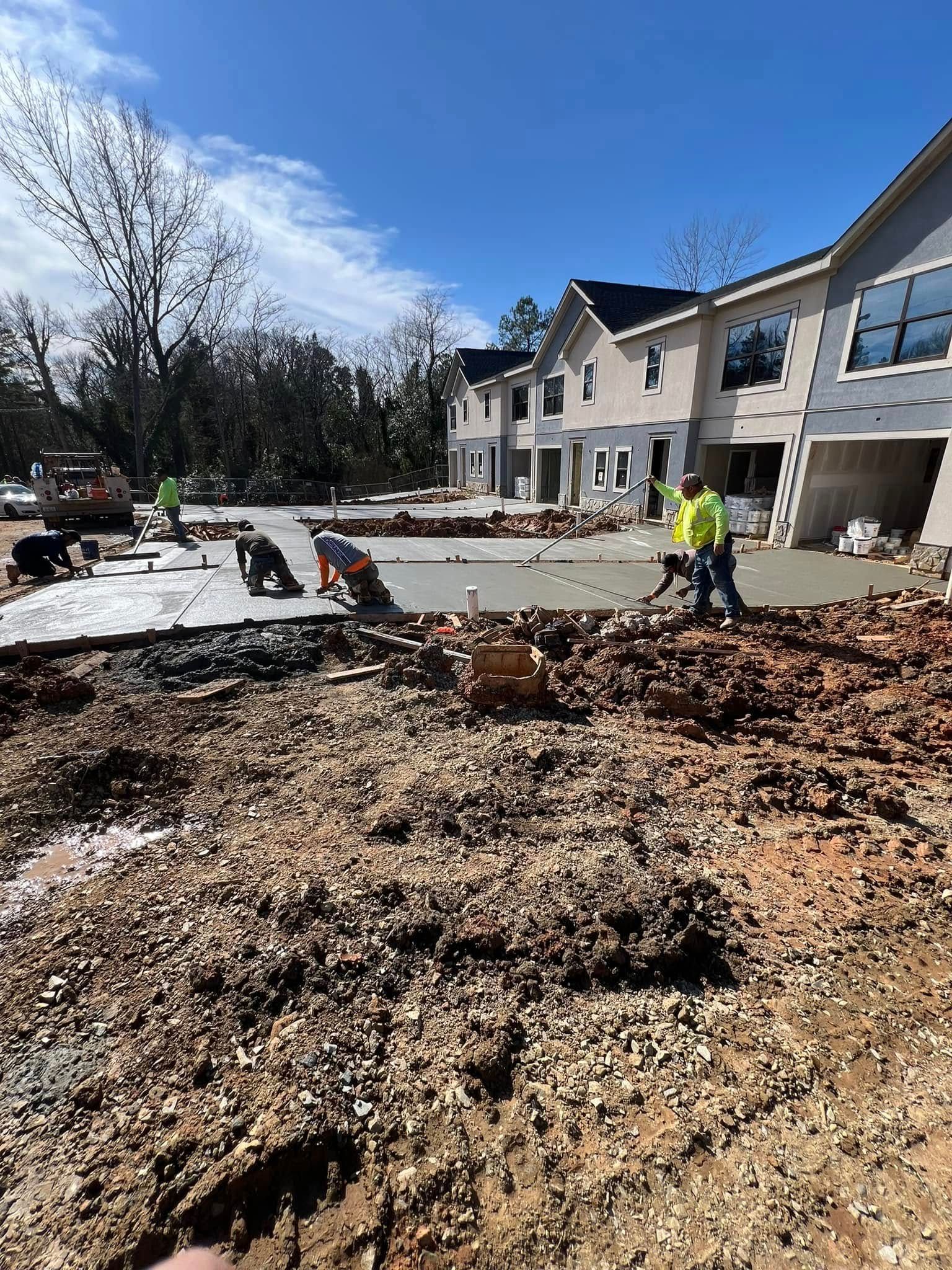 Construction workers pouring concrete on a sunny day. Homes in the background, dirt and gravel in foreground.