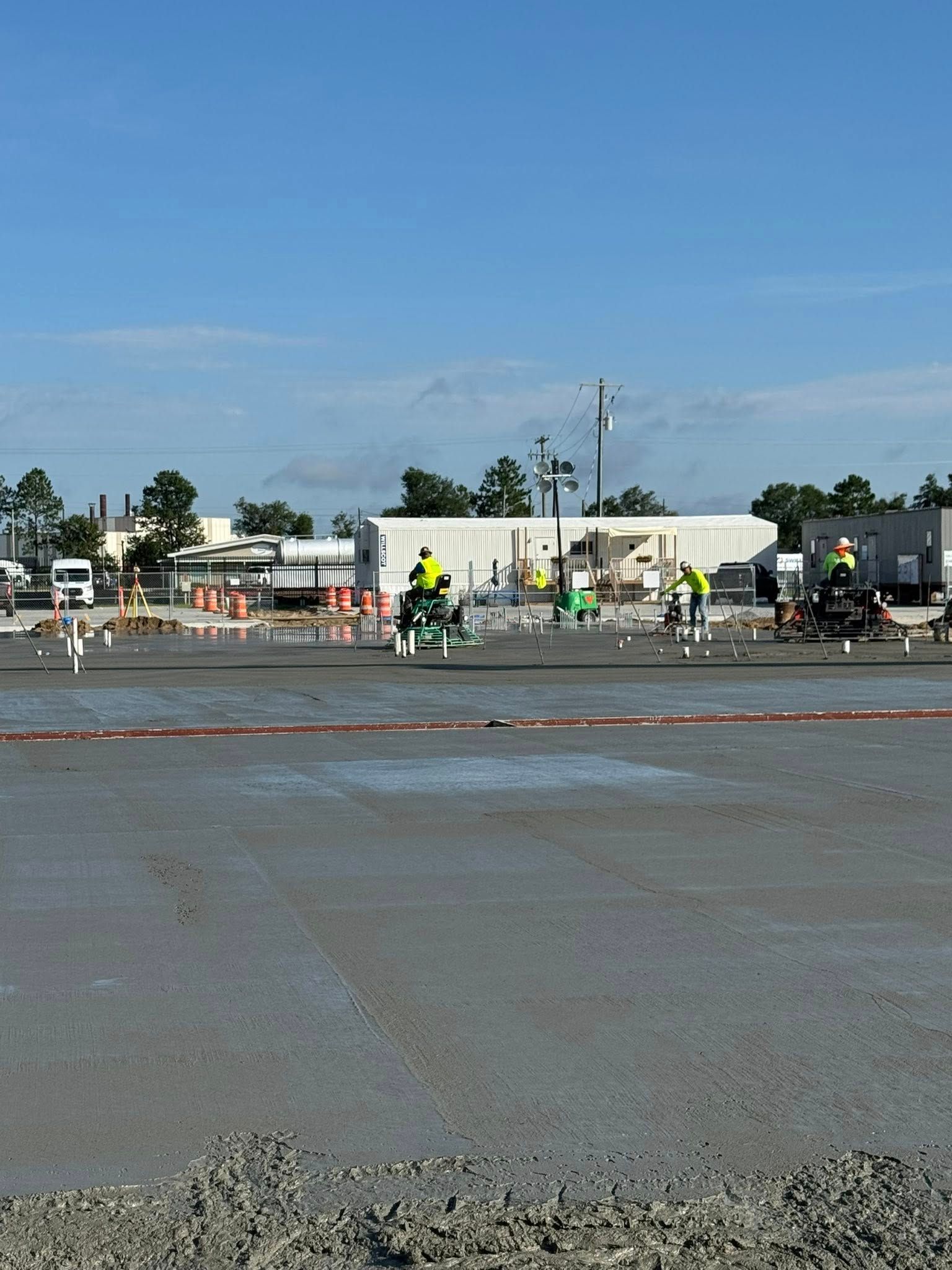 Construction workers smoothing wet concrete at a work site under a blue sky.
