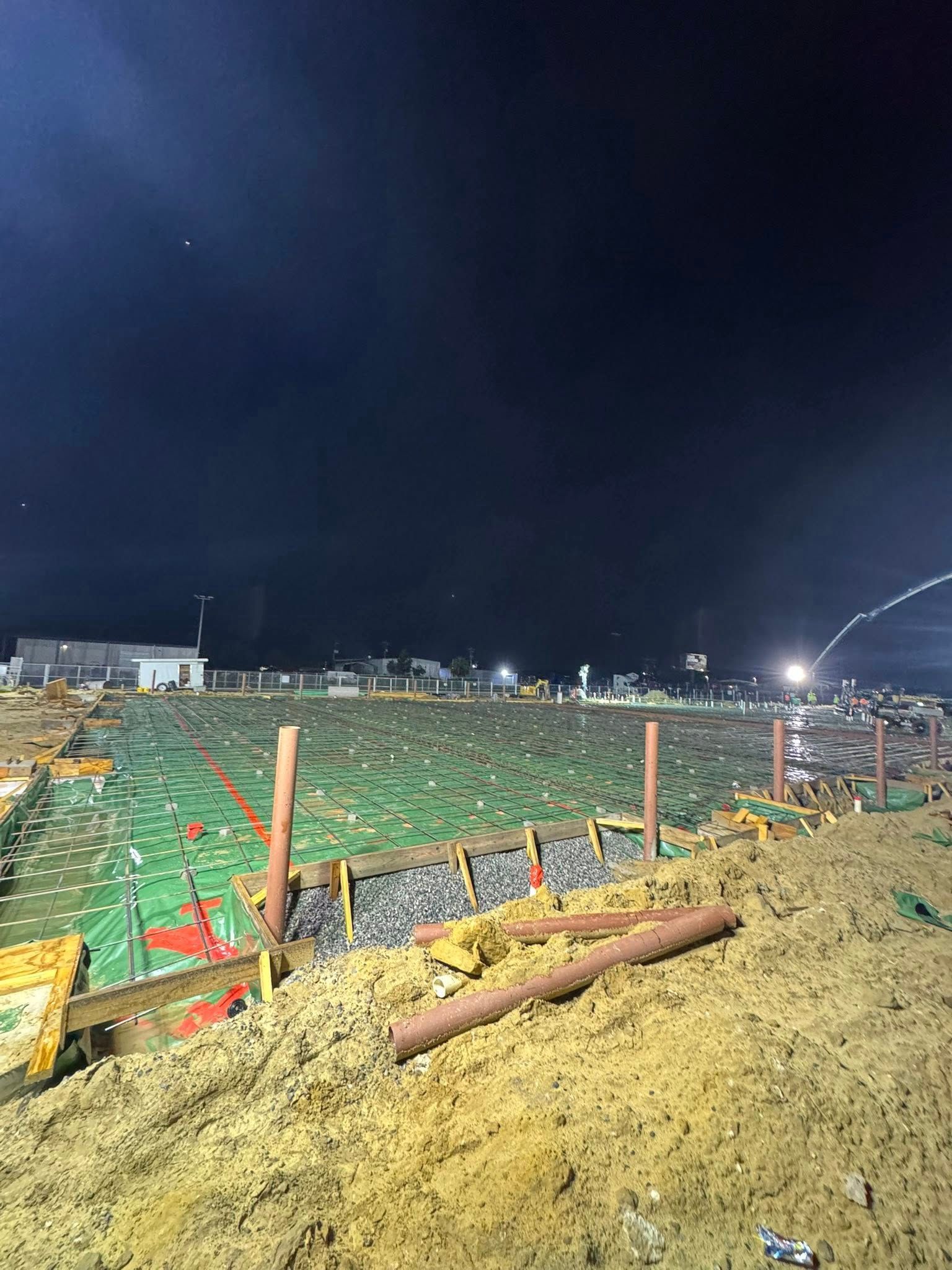 Construction site at night, green insulation, wooden supports, brown soil, dark sky.