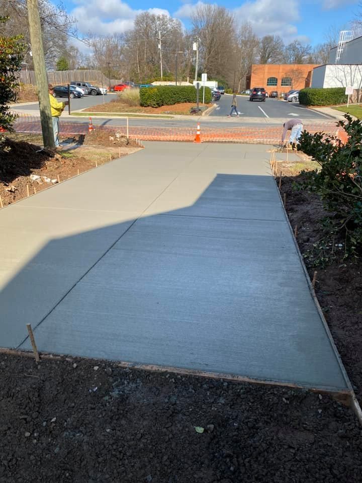 Newly poured concrete walkway, light grey, being smoothed by a worker, construction site, sunny day.