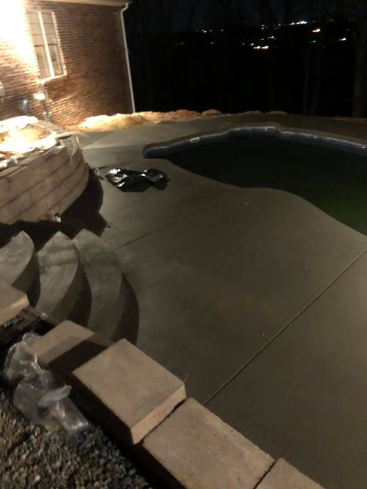 Night view of a pool area with a concrete patio, steps, and surrounding brick wall with landscape lighting.