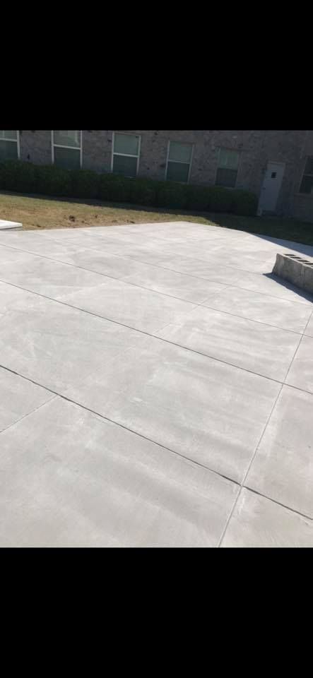 A gray concrete courtyard in front of a brick building, with some grass and a door.
