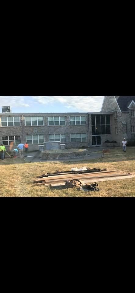 Construction site with building, lawn, and wooden beams. Workers on the steps.