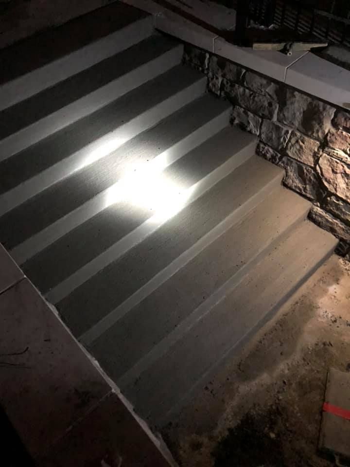 Concrete outdoor staircase illuminated by a bright light. Stone wall to the side.