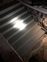 Concrete steps lit from above, leading down to a lower level. Stone wall on the right.