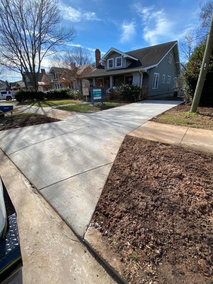 Concrete driveway leading to a gray house with a porch, in a residential neighborhood.
