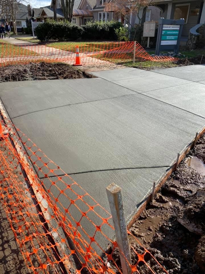 Freshly poured concrete sidewalk with orange safety fencing in front of houses.