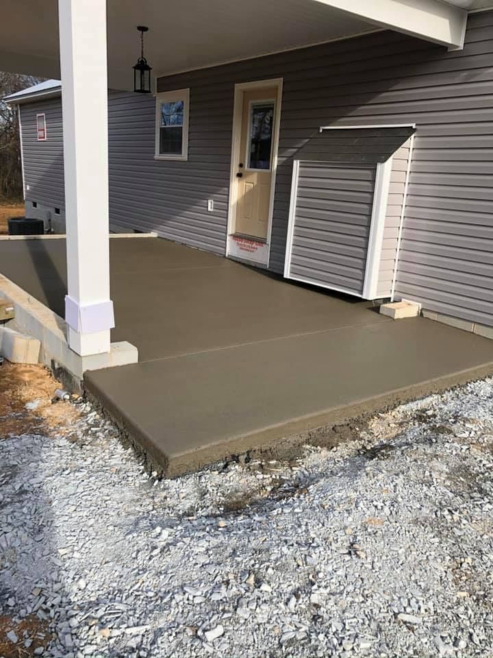 Gray concrete porch next to a house with gray siding, gravel ground.