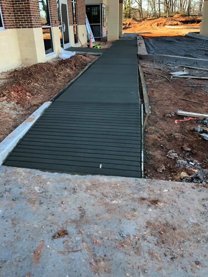 Newly poured concrete ramp and walkway under construction near a building's entrance.