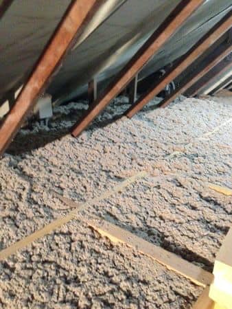 Intérieur du grenier avec isolation épaisse et grise entre les chevrons en bois.