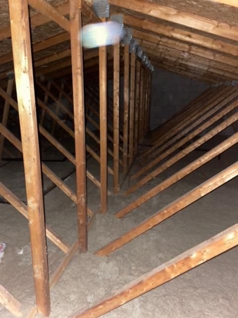 Vue de l'intérieur d'un grenier poussiéreux avec poutres en bois et isolation.