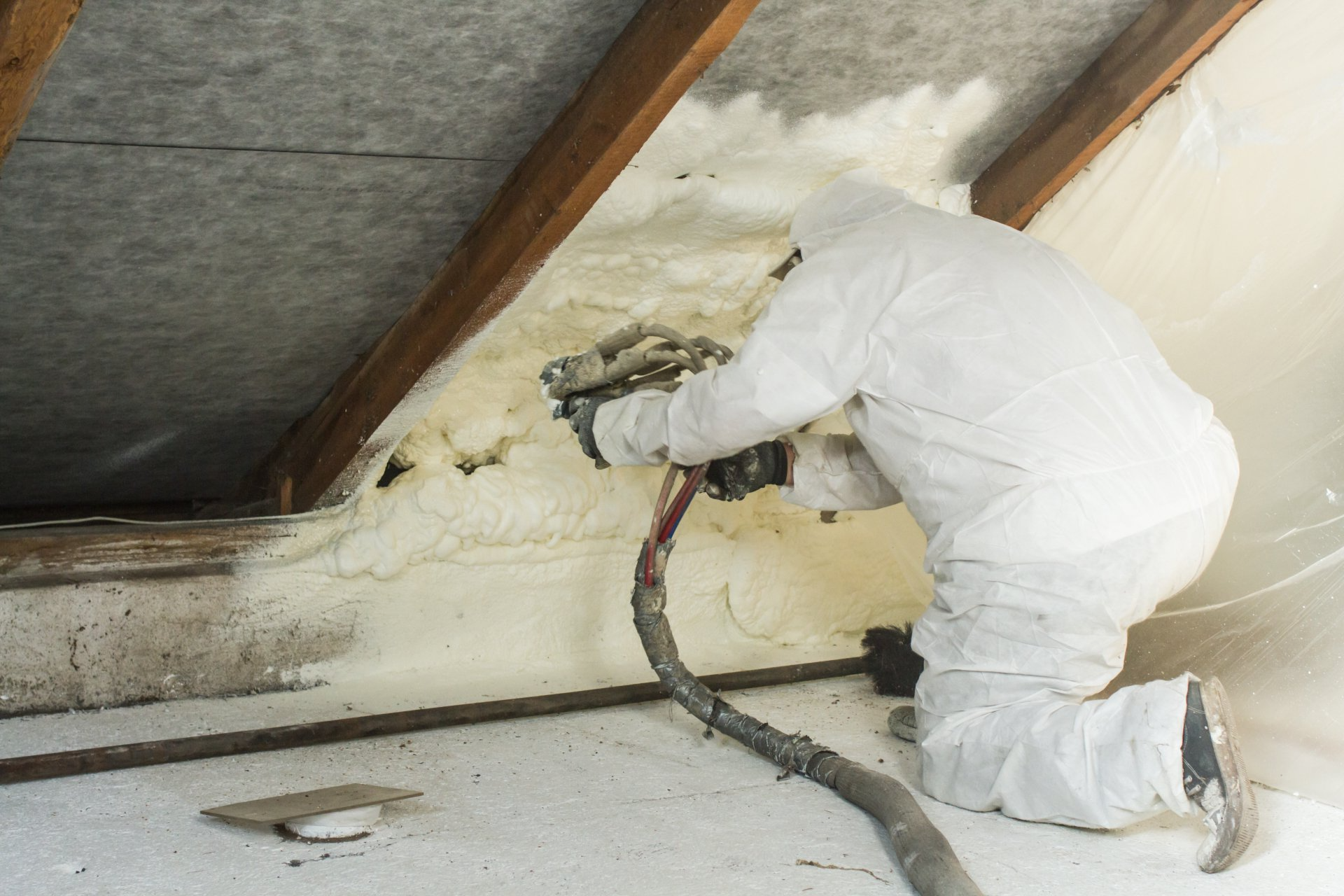 Une personne en combinaison de protection pulvérise de la mousse isolante dans un grenier.
