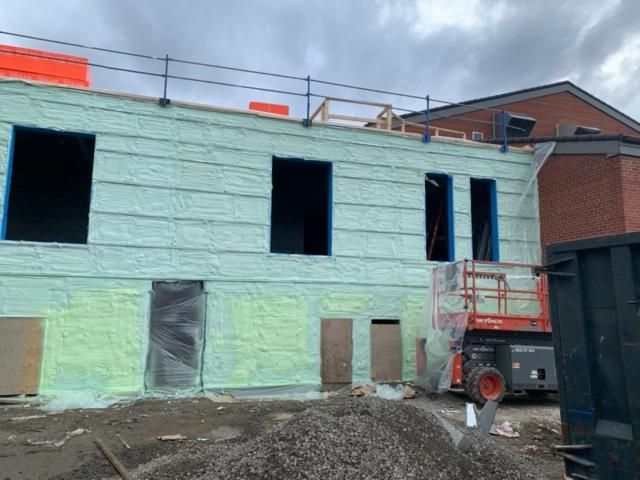 Chantier de construction avec mur isolé vert, fenêtres ouvertes et ascenseur rouge. Ciel nuageux.