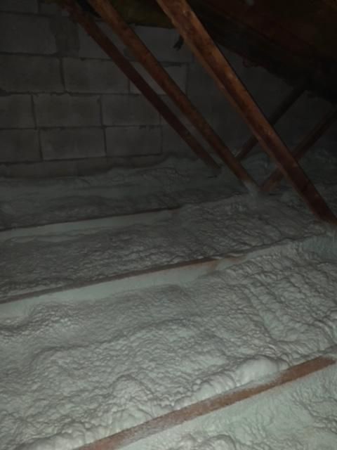 Isolation en mousse pulvérisée blanche dans un grenier entre des chevrons en bois et un mur en parpaings.