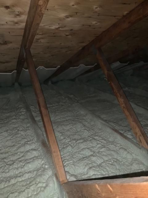 Grenier avec poutres en bois et isolation en mousse blanche recouvrant les chevrons et le plafond.