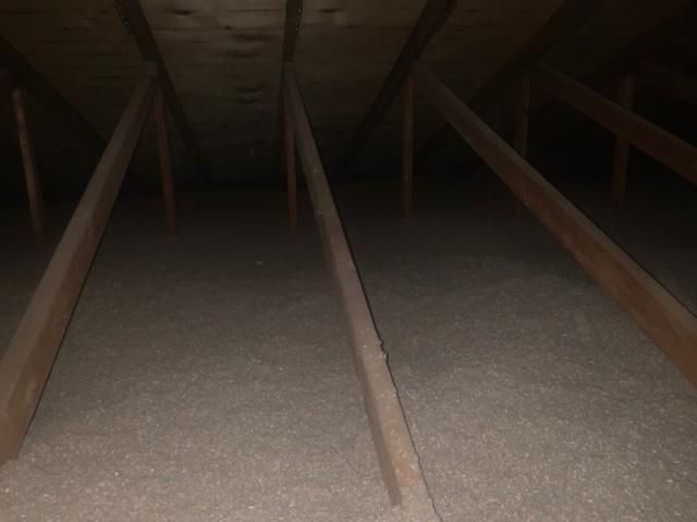 À l'intérieur d'un grenier, poutres en bois inclinées contre une isolation sombre.