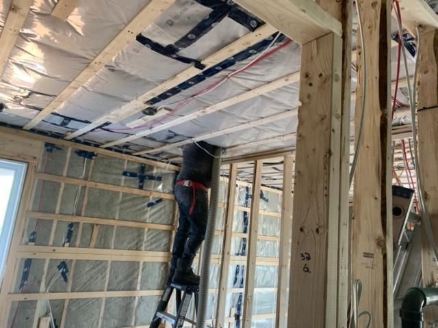 Un homme sur une échelle travaille sur le câblage à l'intérieur d'une pièce à ossature en bois pendant la construction.