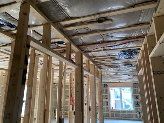 Vue intérieure d'un bâtiment en construction avec ossature en bois et isolation apparente ; la lumière du soleil pénètre à travers une fenêtre.