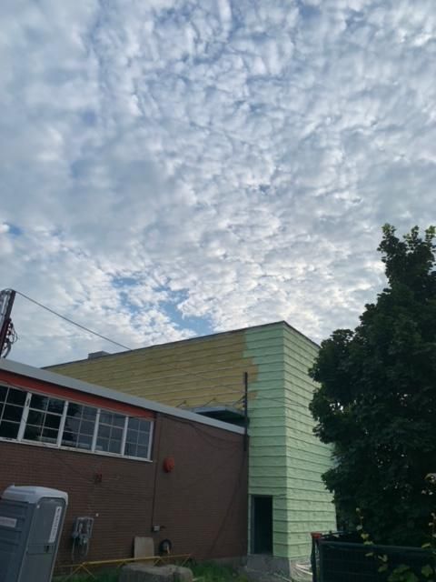 Extérieur du bâtiment avec revêtement vert, ciel nuageux.