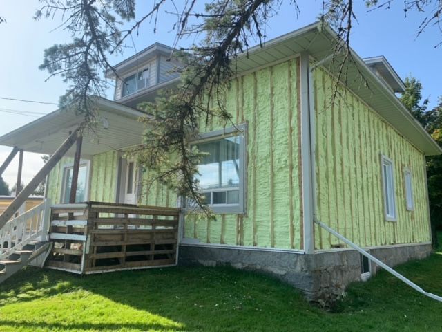 Maison avec murs extérieurs en rénovation; isolation apparente, garniture verte sur blanche.