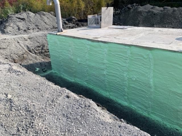 Structure en béton enveloppée de vert en construction ; terrassement, gravier et machinerie en extérieur.